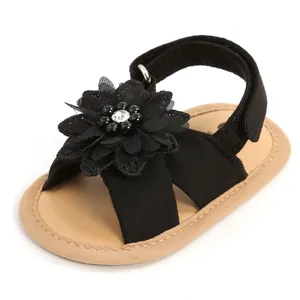 Détail d'une sandale noire pour bébé avec une grande fleur perlée et une semelle souple.
