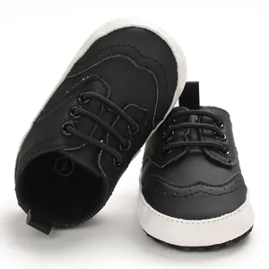 Macro weergave van zwarte baby loopschoenen met brogue details en zachte witte zolen.