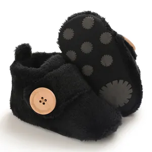 Detailed shot of soft black plush baby shoes showing wooden button and anti-slip sole