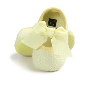 Detail of yellow baby princess shoes with large bow and soft embroidered texture.