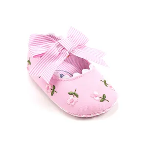 Close-up detail of pink baby girl princess shoes featuring a striped bow and floral embroidery