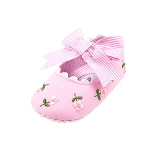 Detailed view of pink embroidered baby shoes with a striped bow and scalloped trim