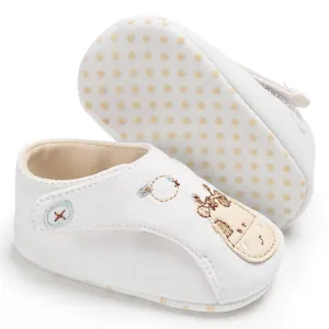 Gros plan de chaussures de marche blanches pour bébé avec semelle souple et girafe.