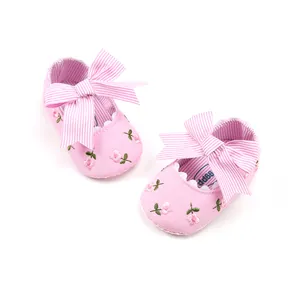 Close-up of pink embroidered baby princess shoes with a large striped bow detail