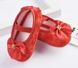 Nahaufnahme roter Satin-Babyschuhe für Mädchen mit Rosenmuster und Schleife.