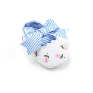 Detailed view of white baby princess shoes with pink floral embroidery and blue striped bow