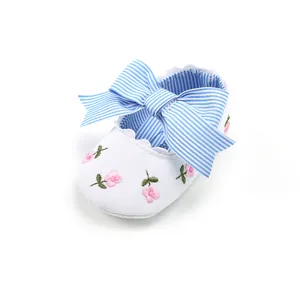 Close-up of white baby princess shoes with pink floral embroidery and a blue striped bow