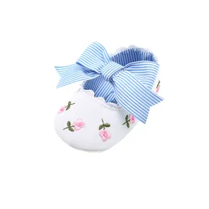 Close-up of pink flower embroidery and blue striped bow on white baby shoe