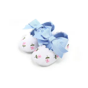 Detail view of white baby princess shoes with pink floral embroidery and blue striped bow