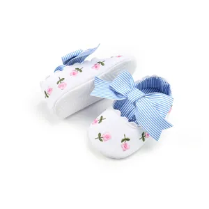 Close-up of white baby princess shoes featuring pink floral embroidery and blue striped bows.