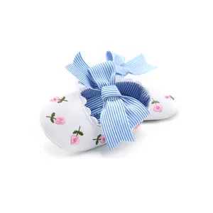 Detail view of baby walking shoes with pink embroidered flowers and a blue striped bow