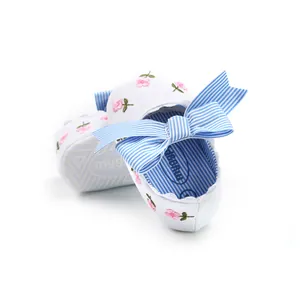 Detailed view of white baby shoes with pink floral embroidery and a blue striped bow