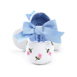 Close-up view of white baby princess shoes featuring floral embroidery and a blue striped bow