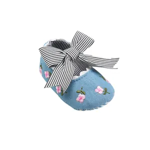 Close-up of baby girl shoes with flower embroidery and striped bow detail.