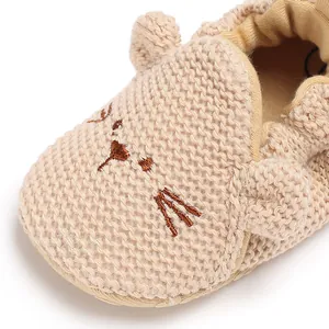 Detailaufnahme eines beigen Strick-Babyschuhs mit süßem gesticktem Katzengesicht