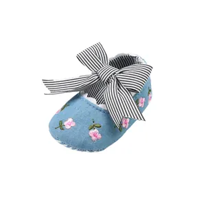Close-up of baby girl's blue denim shoes with pink flower embroidery and striped bow