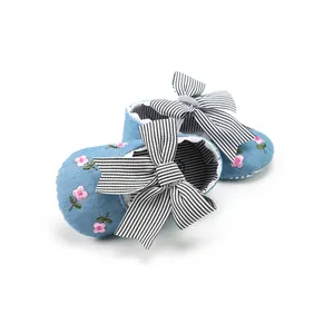 Detail view of blue baby shoes featuring pink floral embroidery and a striped bow