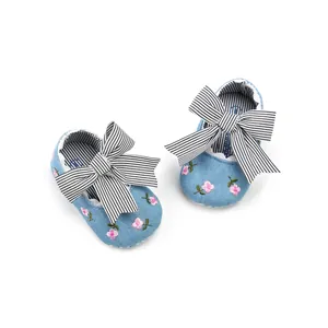 Close-up of soft-sole baby girl shoes featuring pink floral embroidery and a large striped bow