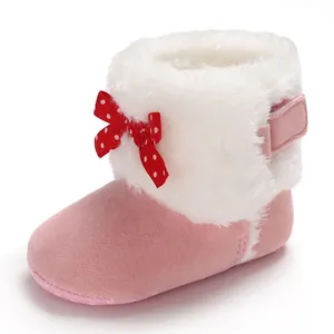 Vista detallada de botas de nieve rosas para bebé con pelo blanco y lazo rojo de lunares.