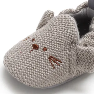 Makroansicht der weichen Strickstruktur und Katzenstickerei auf grauen Baby-Lauflernschuhen