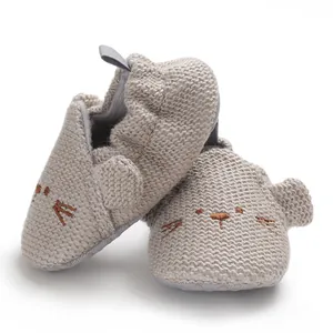 Detailaufnahme der gestrickten Babyschuhe mit weicher beiger Textur und niedlichem Tiergesicht