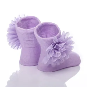 Nahaufnahme von Babysocken mit großen lila Chiffonblumen und weicher Strickstruktur.
