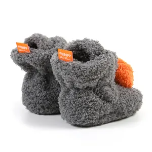 Dettaglio di scarpine per neonati in pile Sherpa grigio con pompon arancioni e etichette
