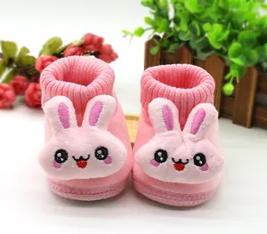 Close-up of pink plush baby booties with cute cartoon rabbit face and ribbed cuffs.