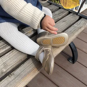 Detail of gold metallic baby walking shoes with soft soles on a wooden bench.