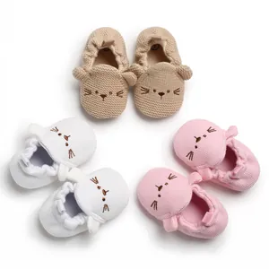 Detailansicht von weiß, rosa und beige gestrickten Babyschuhen mit gestickten Katzenfaces.