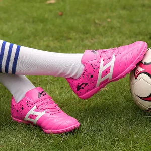 Professional vibrant pink kids' soccer shoes with turf cleats shown on green grass