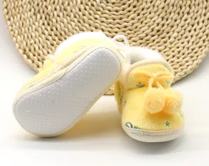 Dettaglio di scarpine in peluche gialle con suola morbida antiscivolo e pompon soffici.