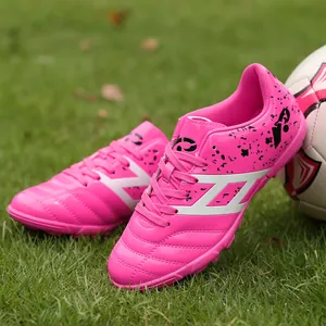 Bright pink kids' soccer shoes with turf cleats on a green grass field