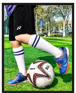 Detailaufnahme blauer Kinder-Fußballschuhe auf grünem Kunstrasen beim Kicken eines Balls