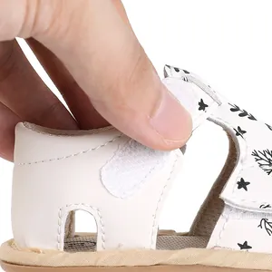 Detailed view of the adjustable hook and loop strap on white patterned baby summer sandals