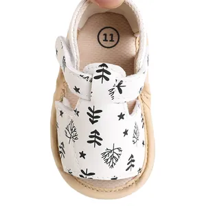 Detail view of white baby sandals featuring black pine tree print and velcro strap