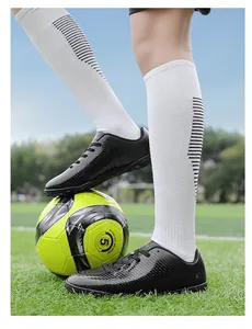 Dettaglio scarpe da calcio per bambini su un campo d'erba con un pallone giallo