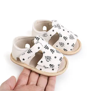 Detailed view of white baby beach sandals with leaf print, held in hand for size comparison.