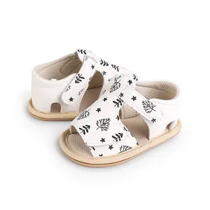 Close-up of white baby walking sandals featuring black leaf prints and Velcro strap.