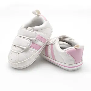 Close-up detail of white infant walking shoes with pink stripes and rubber soles