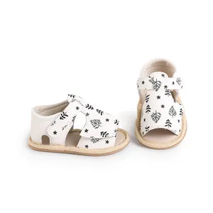 Close-up of white baby summer sandals featuring black botanical leaf and star patterns