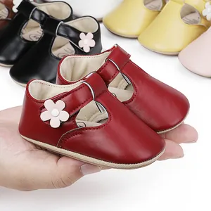 Close-up of red baby Mary Jane shoes with flower detail held in hand for scale.