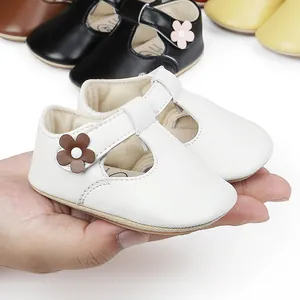 Soft white T-strap baby princess shoes held in hand showing delicate flower detail