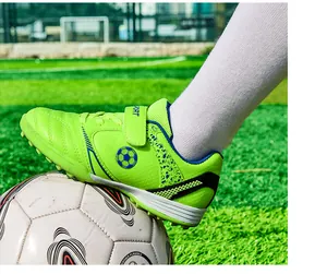 Nahaufnahme von hellgrünen Fußballschuhen für Kinder auf einem Rasenplatz auf Ball
