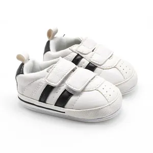 Detailed side view of white baby walker sneakers with black stripes and hook-and-loop straps