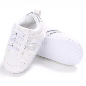 Zapatos de bebé blancos con rayas plateadas y suela suave antideslizante con puntos.