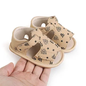 Detail of beige baby sandals with leaf print held on a palm.