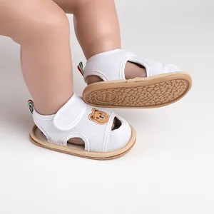 Nahaufnahme von weißen Baby-Sandalen mit Bärenstickerei und rutschfester Sohle.