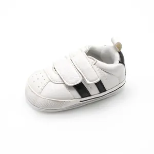 Close-up side view of white baby sneakers featuring two black stripes and velcro straps