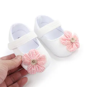Detalle de zapatos blancos de bebé con una flor a cuadros rosa y un botón